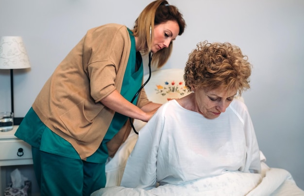 Cuidador feminino auscultando mulher sênior em casa