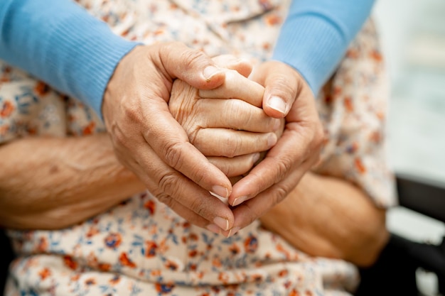 Foto cuidador tomados de la mano paciente anciana asiática con amor, atención, aliento y empatía en el hospital de enfermería concepto médico fuerte y saludable