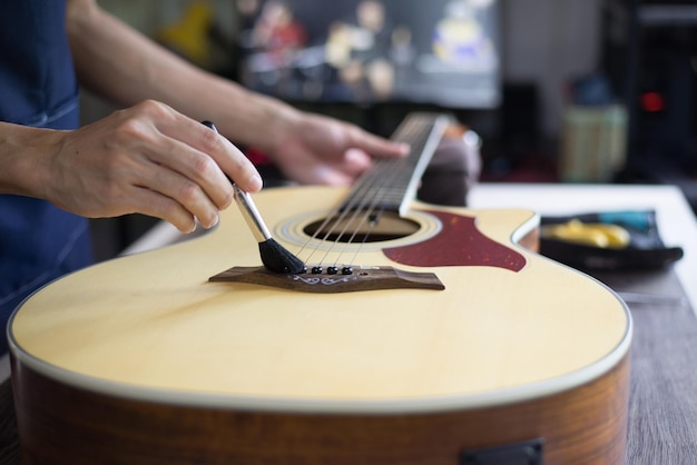 Cuidados com a guitarra acústica O artesão está limpando a guitarra com escova de limpeza Fechar