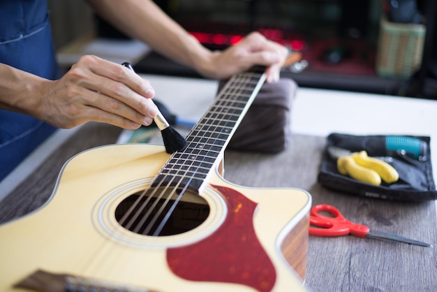 Cuidados com a guitarra acústica O artesão está limpando a guitarra com escova de limpeza Fechar