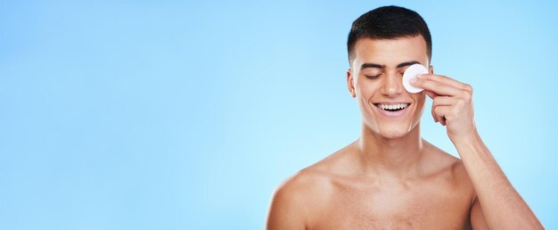 Cuidados com a pele de almofada de algodão e homem em fundo azul para bem-estar, pele saudável e cuidados faciais dermatologia banner maquete de beleza e pessoa com patch para preparar cosméticos e higiene facial em estúdio