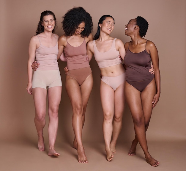 Cuidados com a pele de beleza e diversidade de mulheres com abraço e sorriso para saúde, bem-estar e confiança Grupo de modelos naturais e cosméticos para cuidados com o corpo em roupas íntimas para campanha inclusiva no estúdio marrom