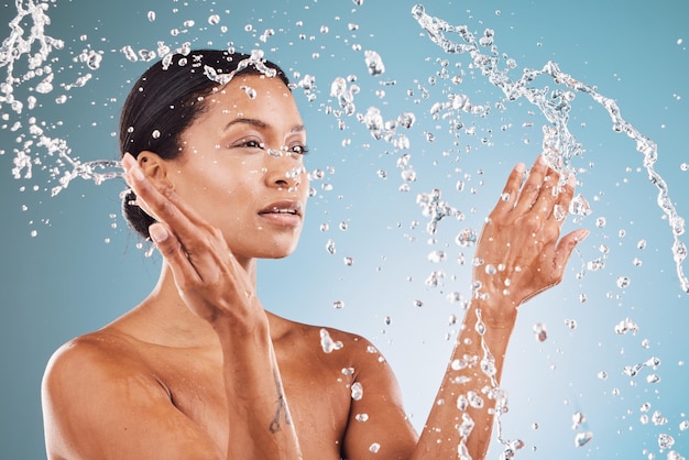 Cuidados com a pele de beleza e mulher negra com respingos de água para limpeza de higiene e rotina de cuidados com o corpo Autocuidado bem-estar e pele saudável do modelo pensando com respingos de água no estúdio azul