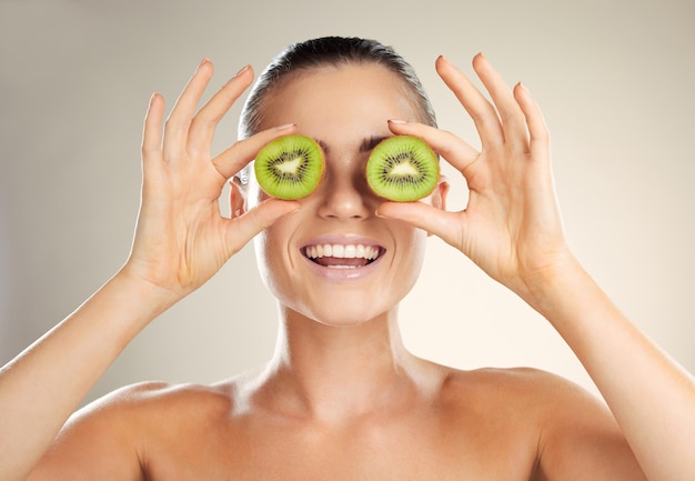 Cuidados com a pele de frutas kiwi e beleza de cobertura por uma mulher com produto cosmético de dermatologia natural Brilho saudável no rosto de modelo estético em estúdio para máscara facial de spa sustentável para saúde e bem-estar