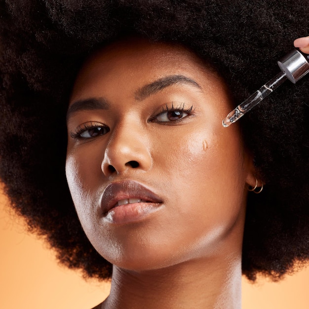 Cuidados com a pele de óleo e mulher negra com produto para rosto contra um fundo de estúdio laranja Retrato de um jovem modelo africano e cosmético com soro líquido para saúde facial beleza e bem-estar da pele