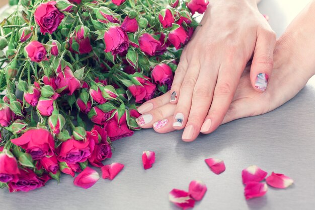 Cuidados com a pele de uma linda mulher mãos com arte unha manicure. E mesa cinza com pequenas rosas rosa