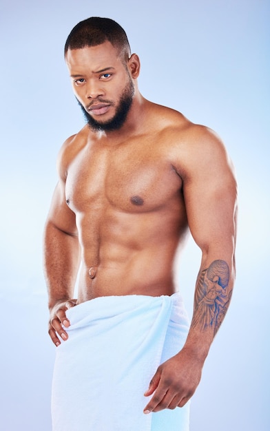 Foto cuidados com a pele do retrato e corpo com um homem em fundo branco e vestindo uma toalha no estúdio após a limpeza higiene aliciamento e sério modelo masculino africano musculoso posando sem camisa em seu banheiro