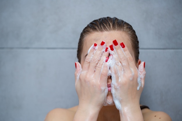 Cuidados com a pele do rosto. mulher aplicando limpador facial no rosto closeup. menina usando produto cosmético de limpeza na pele, lavando o rosto em fundo claro