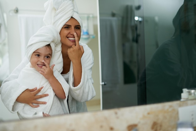 Cuidados com a pele espelho e mãe com a menina na casa de banho para a ligação higiene e juntos para a rotina matinal Dermatologia família e mãe com criança em casa com produtos de beleza cosméticos e loção