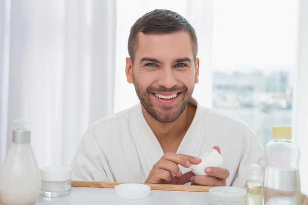 Cuidados com a pele. homem alegre e simpático segurando uma garrafa de creme enquanto cuida de sua pele