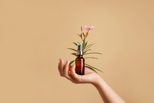 Cuidados com a pele Uma bela mão feminina segura uma garrafa de vidro castanho de cosméticos de cuidados com flores