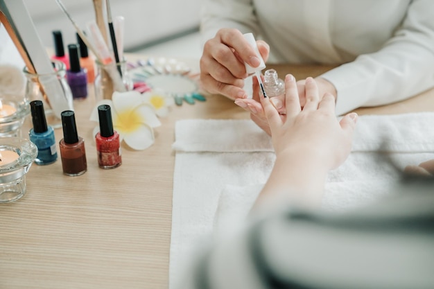 Cuidados com as unhas e manicure. Closeup de belas mãos femininas aplicando esmalte transparente no serviço de atendimento domiciliar. mulher manicure pintando unhas de cliente senhora dentro de casa em pano branco na mesa