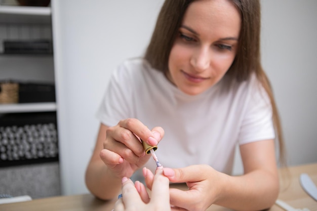 Cuidados com as unhas e manicure. Mulher aplicando esmalte nas unhas da mulher natural saudável no salão de beleza.