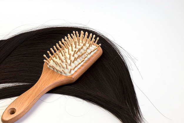 Cuidados com o cabelo pente de madeira em um longo fio de cabelo preto em um fundo branco Ferramentas de materiais biológicos e cabelo natural