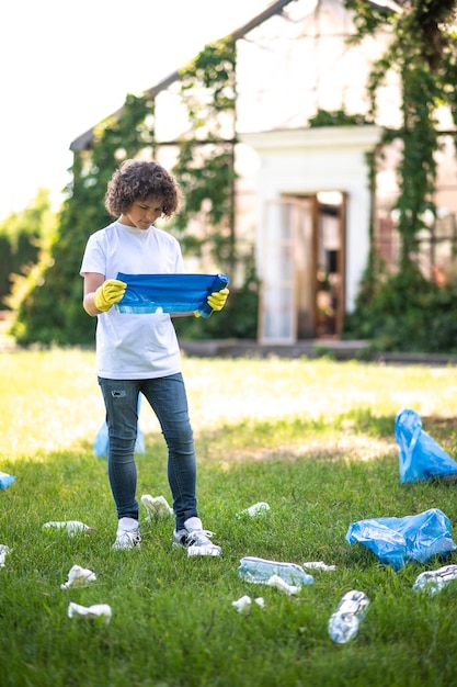 Foto cuidados com o meio ambiente. adolescente de camisa branca em pé na grama entre garrafas plásticas