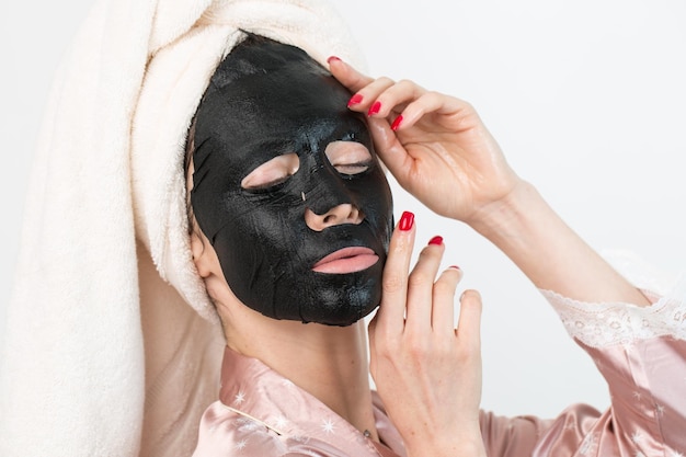 Foto cuidados com o rosto e tratamentos de beleza mulher com uma máscara de carvão hidratante de folha no rosto isolado no fundo branco
