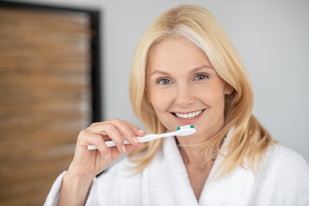 Cuidados com os dentes. Mulher loira sorridente, escovando os dentes e parecendo feliz