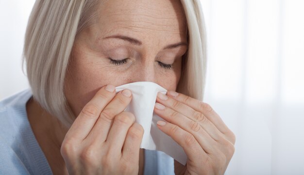 Cuidados de saúde, frio, alergia e mulher doente assoar o nariz escorrendo em papel absorvente.