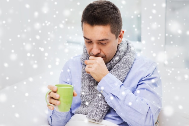 Foto cuidados de saúde, pessoas, inverno e conceito de medicina - homem doente com gripe, tosse e bebendo chá quente da xícara em casa sobre o efeito da neve