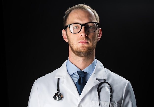 cuidados de saúde, pessoas, profissão e conceito de medicina - close-up do médico de jaleco branco com estetoscópio sobre fundo preto