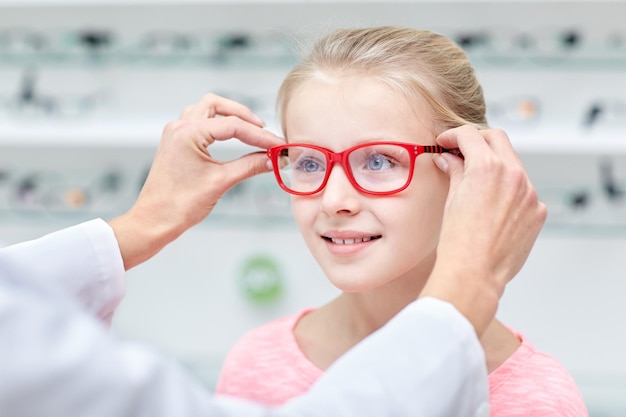 cuidados de saúde, pessoas, visão e conceito de visão - oftalmologista colocando óculos para os olhos da menina na loja de óptica