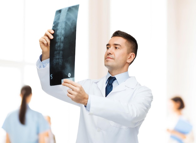 cuidados de saúde, roentgen, pessoas e conceito de medicina - médico de jaleco branco olhando para o raio-x sobre o grupo de médicos no fundo do hospital