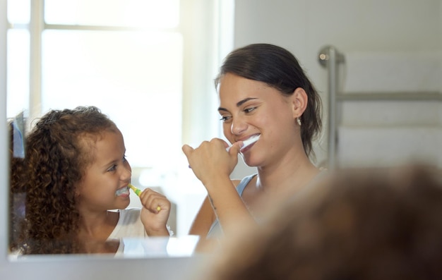 Foto cuidados dentários, escovar os dentes e rotina saudável na manhã da mãe e da filha em casa, criança divertida e brincalhona e vínculo dos pais e aprendendo higiene e higiene com pasta de dente em um banheiro