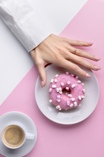 Cuidados de la mano de mujer con blanco taza de café y donas