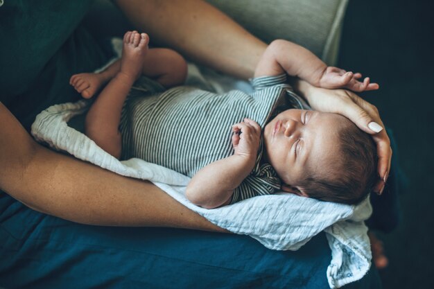 Foto cuidadosa mãe caucasiana segurando seu bebê recém-nascido nas pernas enquanto ela está dormindo