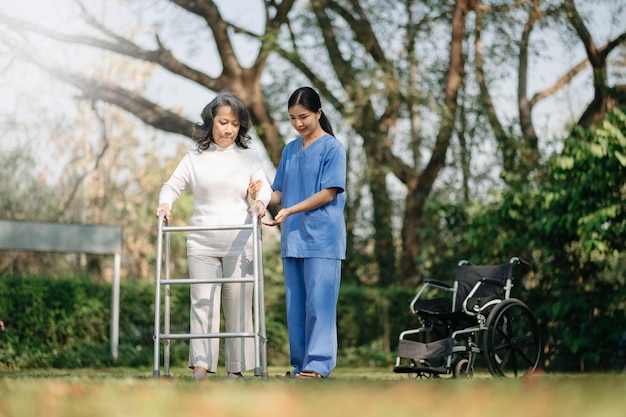 El cuidadoso cuidador o enfermera asiático y el feliz paciente en silla de ruedas caminan por el jardín para