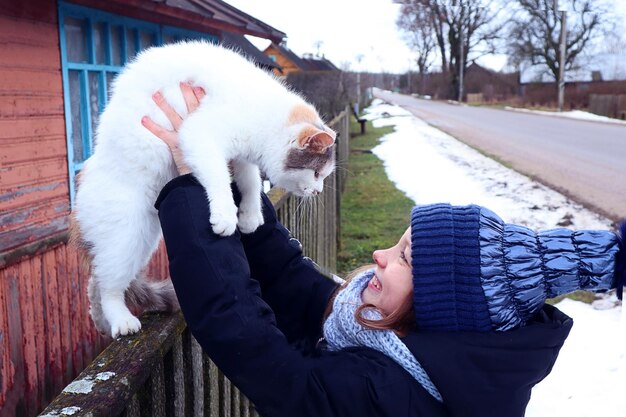 Cuidamos de las mascotas una niña sonriente de diez años con una gorra azul saca un gato blanco de la valla de un pueblo