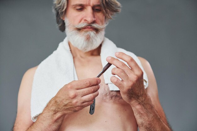 Cuidando la barba El hombre mayor moderno y elegante con canas está en el interior