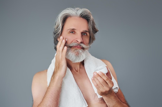 Cuidando la claridad de la cara y la piel El hombre mayor moderno y elegante con cabello gris y barba está en el interior