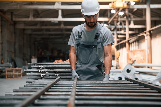 Foto cuidando de produtos metálicos jovem trabalhador de fábrica de uniforme cinzento