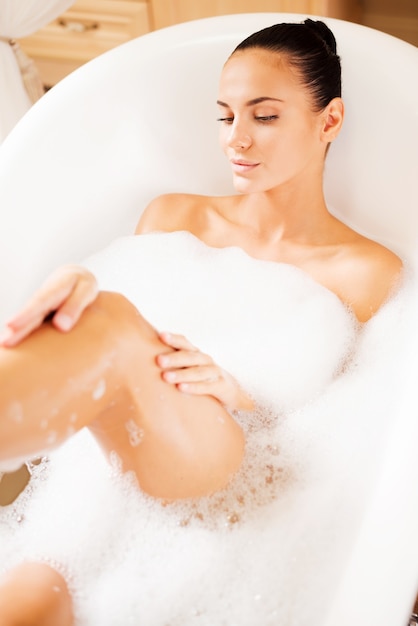 Cuidando de sua pele. Vista superior de uma bela jovem tocando sua perna enquanto desfruta de um banho luxuoso