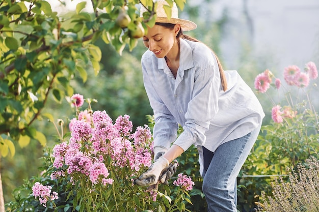 Cuidando las flores La joven mujer alegre está en el jardín durante el día