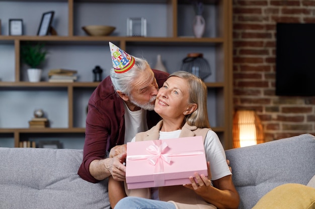 Foto cuidando a un viejo esposo dando un romántico regalo de cumpleaños a una emocionada esposa madura que ama a un hombre mayor sorpresa