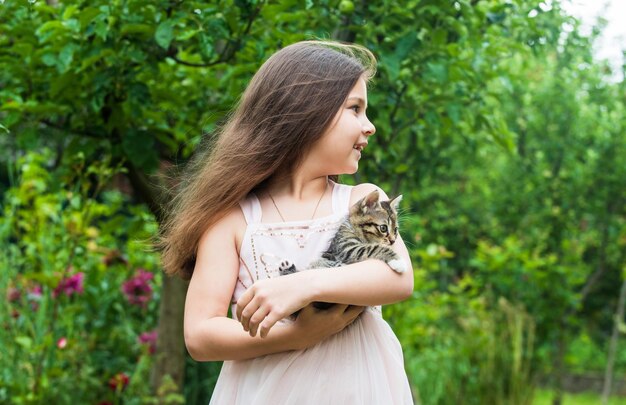 Cuidaré de ti, pequeña niña, sostén un lindo gato en las manos, un niño ama a su mascota, humanos y animales, aman y cuidan a un gatito esponjoso en la mano de un niño bonito, pequeña belleza al aire libre con una mascota, infancia feliz.