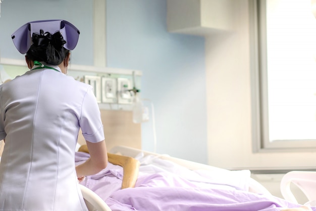 Cuide cuidando al paciente masculino mayor en una habitación de hospital con luz del sol en la ventana.