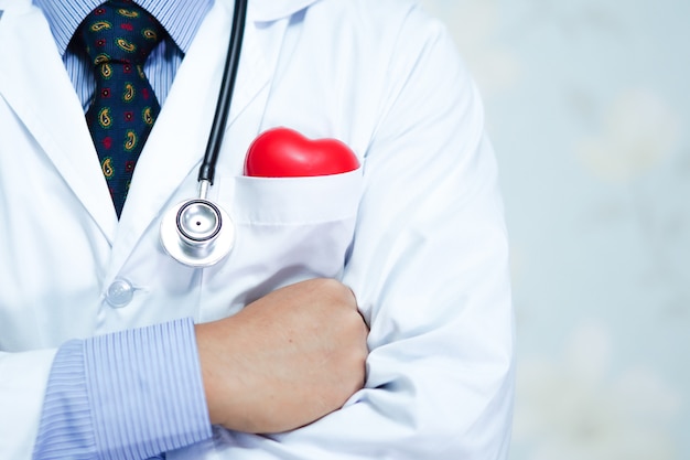 Cuide llevar a cabo el corazón rojo en su bolso de la camisa con el estetoscopio en hospital.