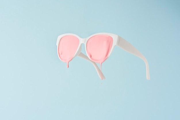 Óculos brancos com tinta rosa pingando sobre um fundo azul Um conceito criativo de verão