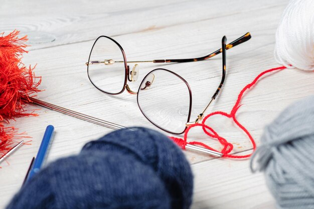 Óculos com fios para tricotar em um conceito de acessórios de tricô de mesa de madeira branca