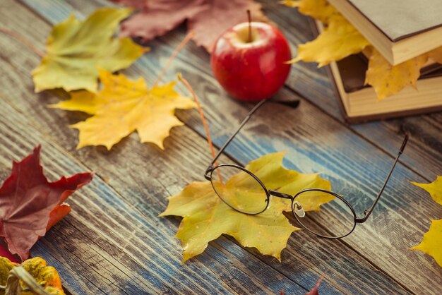 Óculos com livro e folhas de outono na mesa