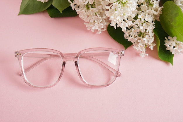 Óculos da moda e um ramo de lilás branco em um fundo rosa, óculos e flores, moldura transparente para óculos