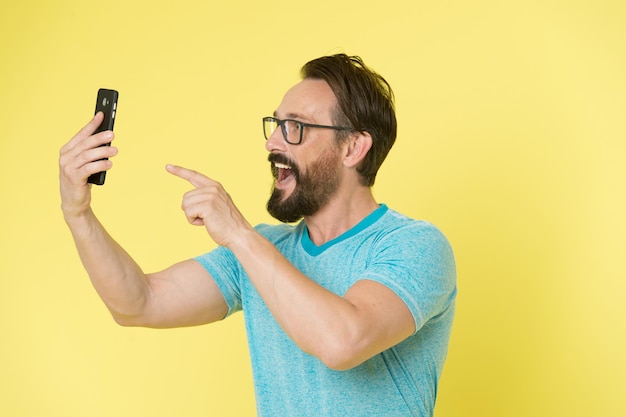 Óculos de cara alegre apontando para smartphone. Homem feliz usuário interagir aplicativo para smartphone. Cara barbudo interagir aplicativo de interface móvel. Homem animado com novas oportunidades.