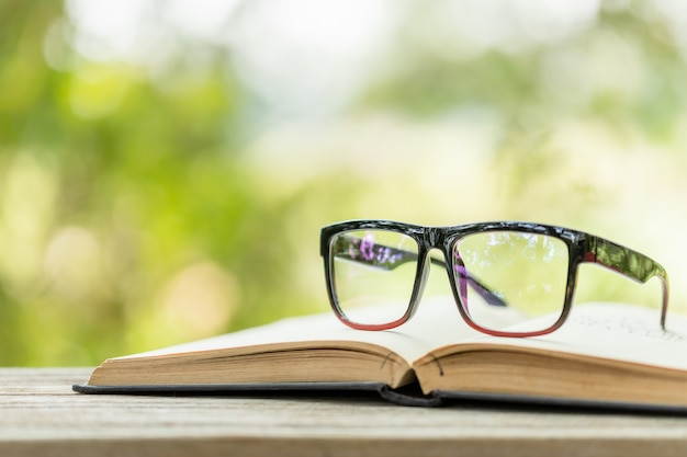 Óculos de livro e olho na mesa de madeira com natureza verde abstrata blur conceito de leitura e educação