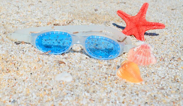 Óculos de mar com estrela do mar e conchas em uma praia branca