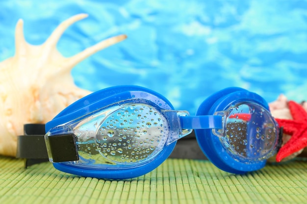 Óculos de natação azul com gotas em uma almofada de bambu no fundo do mar azul