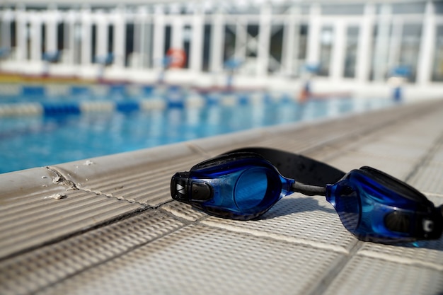 Óculos de proteção azuis para nadar na lateral da piscina