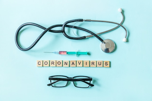 Óculos de seringa e estetoscópio de Coronavirus de frase de texto na parede azul pastel. Novo conceito de vacina contra o coronavírus 2019-nCoV MERS-Cov covid-19 no Oriente Médio com a síndrome respiratória do vírus da coronavírus.